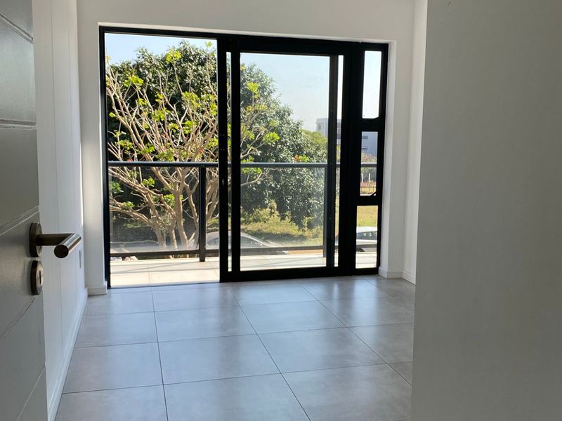 A bright, empty room featuring large black-framed sliding glass doors that open onto a private balcony with outdoor views.