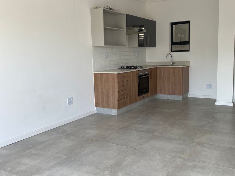 Open-plan kitchen featuring modern wood-look cabinetry, built-in oven, gas hob, extractor fan, and tiled flooring in a neutral, well-lit space.