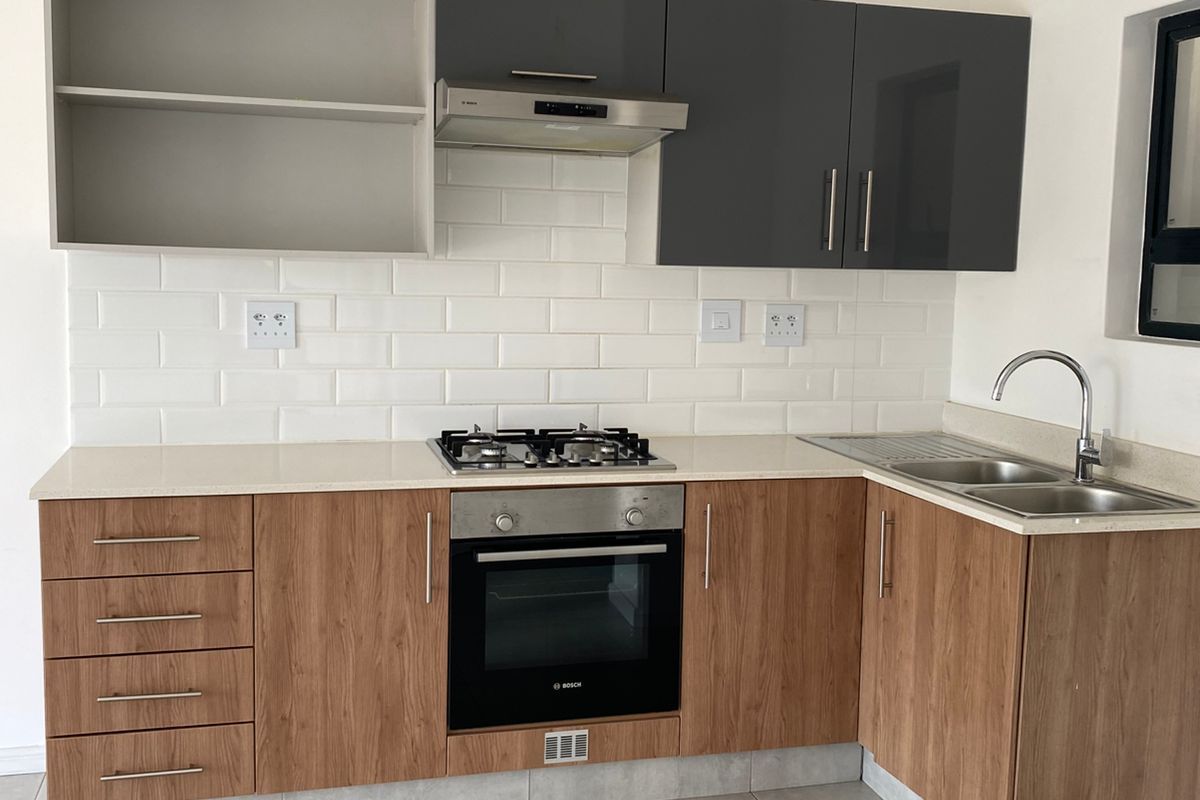 Modern kitchen featuring wood-look cabinetry, contrasting grey upper cabinets, white subway tile backsplash, built-in oven, gas hob, and stainless steel sink.