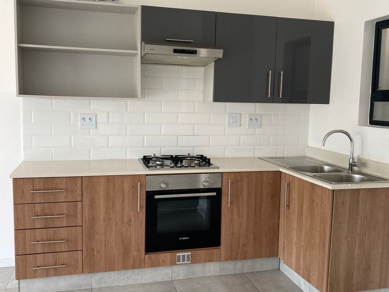 Modern kitchen featuring wood-look cabinetry, contrasting grey upper cabinets, white subway tile backsplash, built-in oven, gas hob, and stainless steel sink.