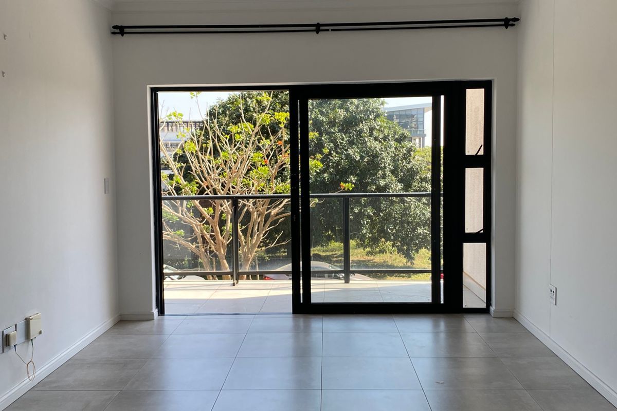 A bright, empty living area featuring large sliding glass doors that open onto a private balcony with outdoor views.