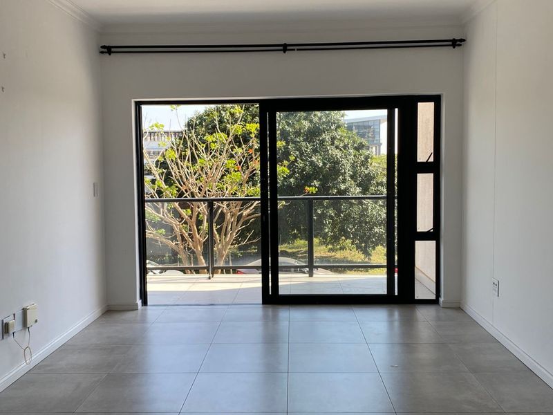 A bright, empty living area featuring large sliding glass doors that open onto a private balcony with outdoor views.