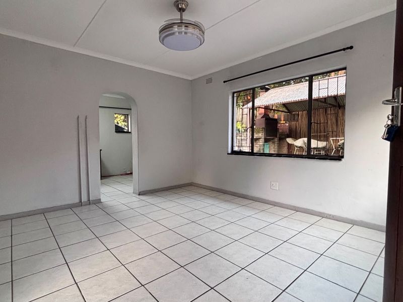 An empty living room featuring neutral tiled flooring, a ceiling fan, and an arched doorway leading to an adjacent space.