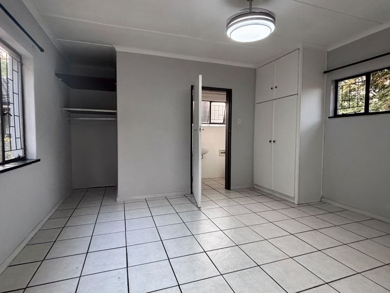A vacant bedroom featuring tiled flooring, built-in cupboards, and security bars on the windows, offering a clean and functional space.