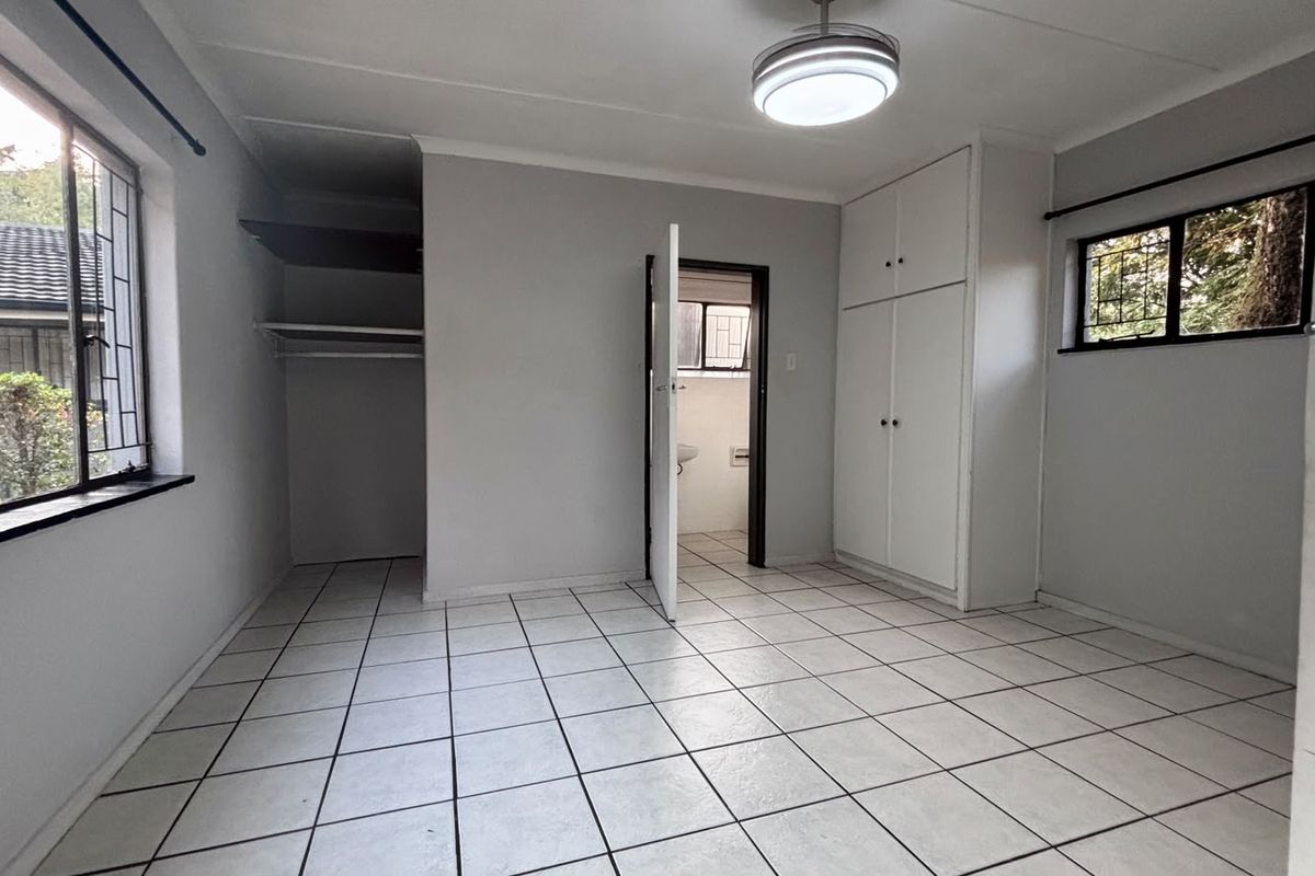 A vacant bedroom featuring tiled flooring, built-in cupboards, and security bars on the windows, offering a clean and functional space.