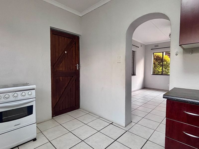 A functional kitchen area featuring tiled flooring, built-in cabinetry, and a freestanding stove, leading through an archway into an adjacent living space.