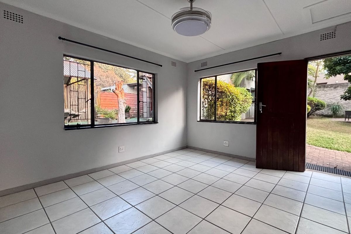 A bright, empty living room featuring neutral tiled flooring, large windows providing natural light, and direct access to the garden area.