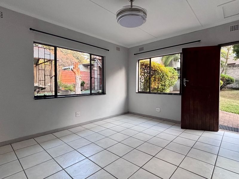 A bright, empty living room featuring neutral tiled flooring, large windows providing natural light, and direct access to the garden area.
