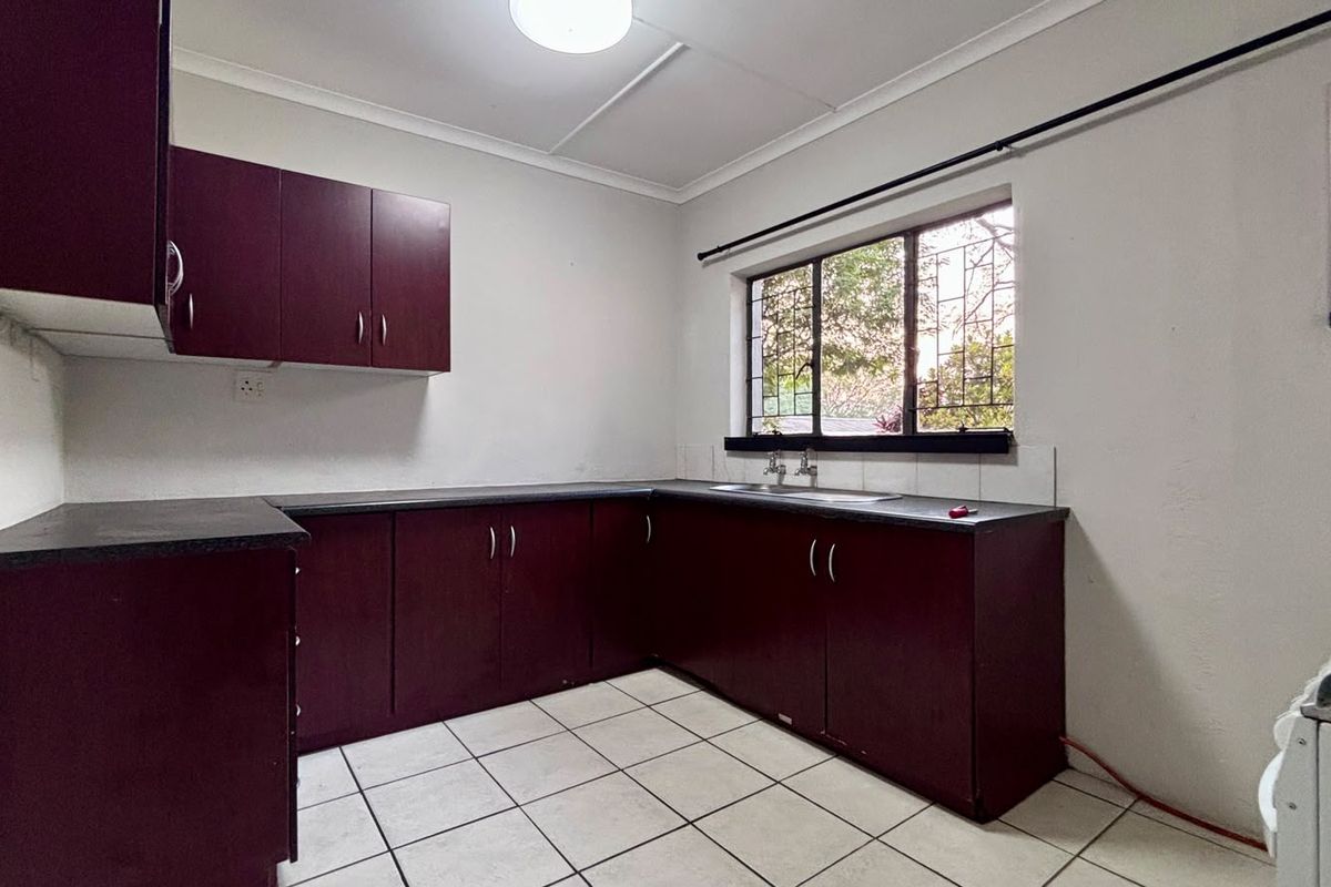 A functional kitchen featuring dark laminate cabinetry, contrasting countertops, tiled flooring, and a window with security bars.
