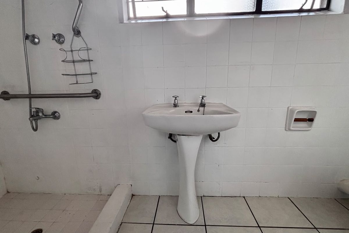 A functional bathroom featuring a pedestal basin, shower area with grab rail, and tiled finishes, requiring cosmetic updates to improve its overall condition.