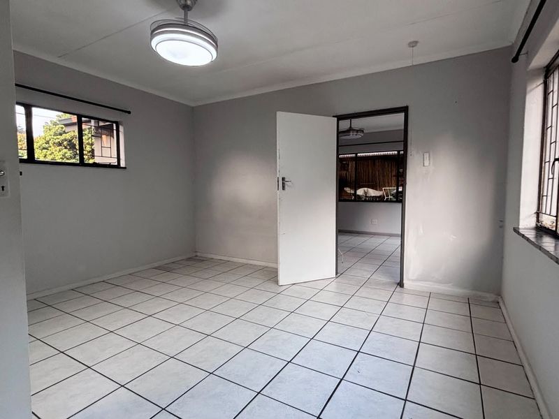 An empty bedroom featuring tiled flooring, security bars on the windows, and a central ceiling light fixture, ready for personalization.