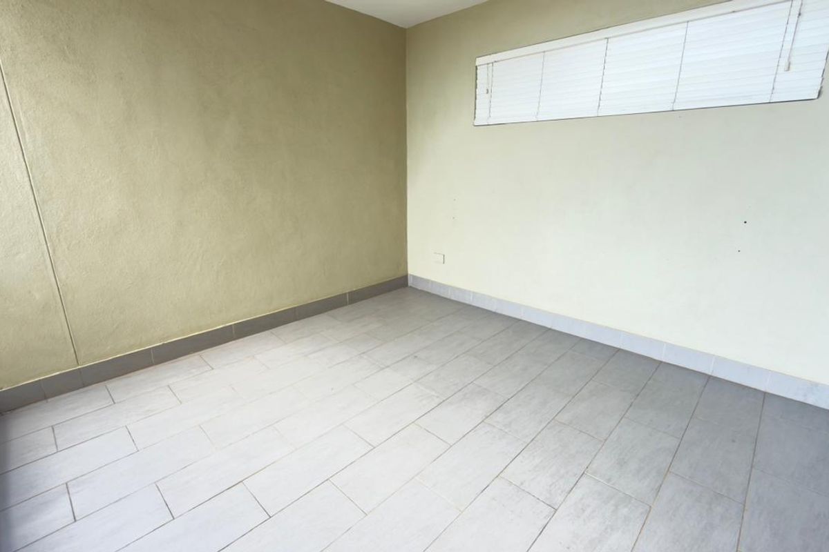 An empty, neutral-toned room featuring tiled flooring and a high-set window with fitted blinds, offering a blank canvas for various uses.
