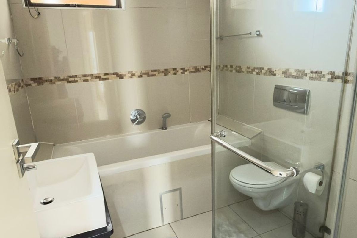 A modern bathroom featuring a wall-mounted toilet, a glass-enclosed shower, a bathtub, and a vanity basin with neutral wall tiling.