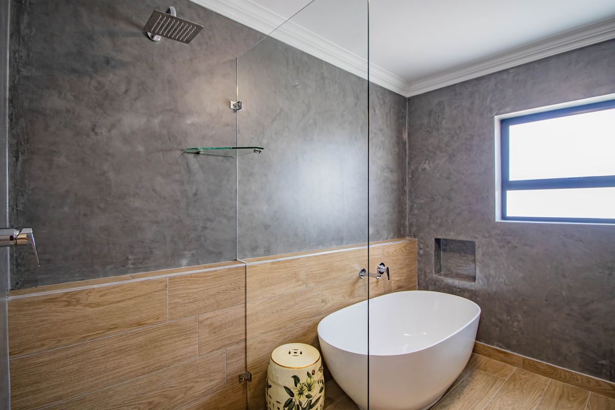 Modern bathroom featuring a freestanding bathtub, glass shower screen, rainfall showerhead, and a combination of concrete-look wall finishes and wood-look floor tiles.
