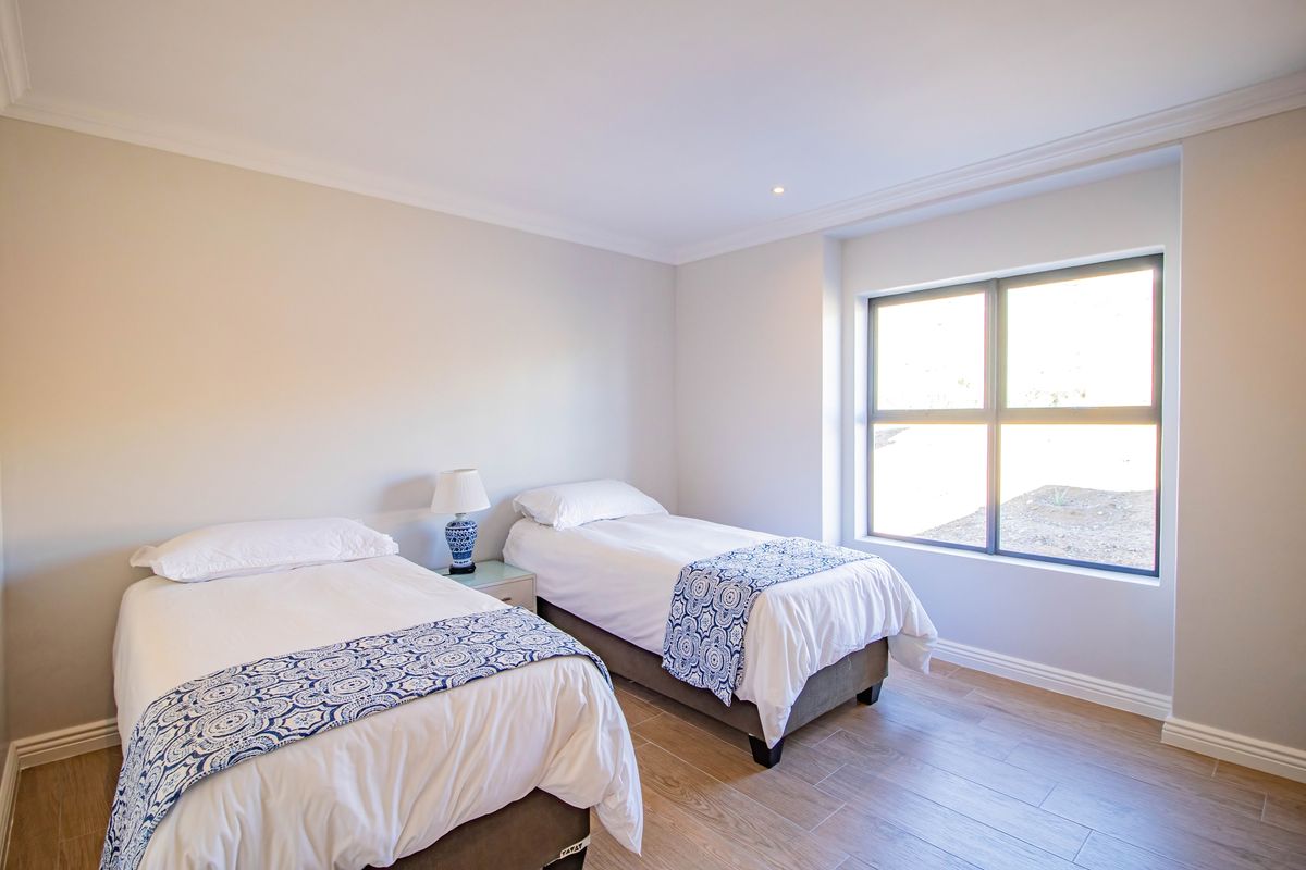 A bright and well-maintained bedroom featuring neutral wall tones, wood-look tiled flooring, and a large window providing natural light.