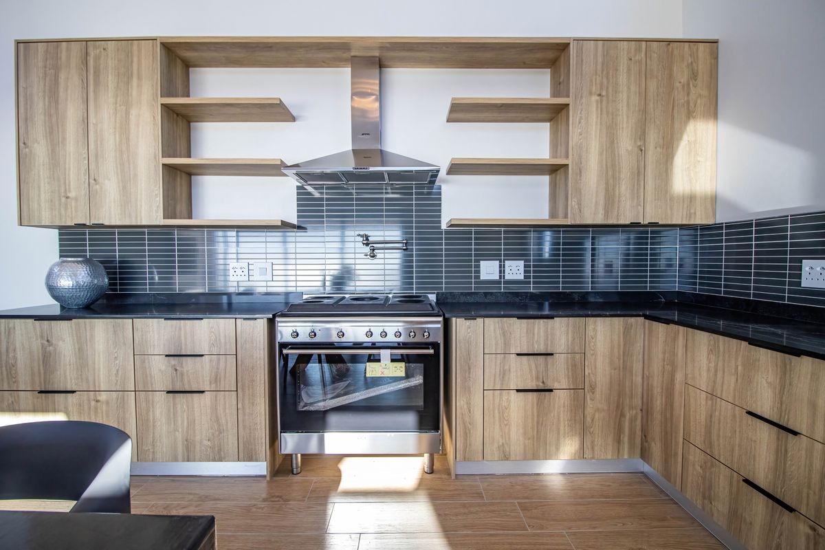 Modern kitchen featuring wood-grain cabinetry, dark stone countertops, a stainless steel freestanding oven with extractor fan, and a sleek subway tile backsplash.