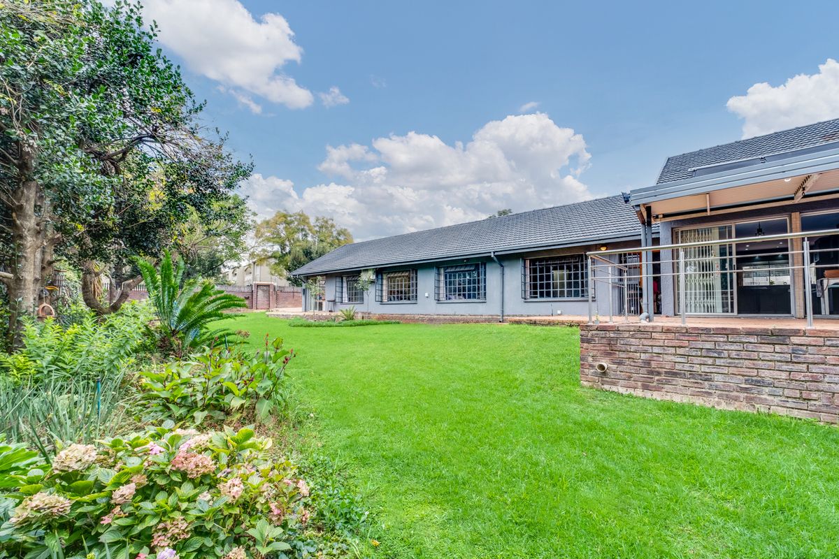 Rear view of the house featuring a well-maintained lawn, landscaped garden, and a brick patio with stainless steel railings.