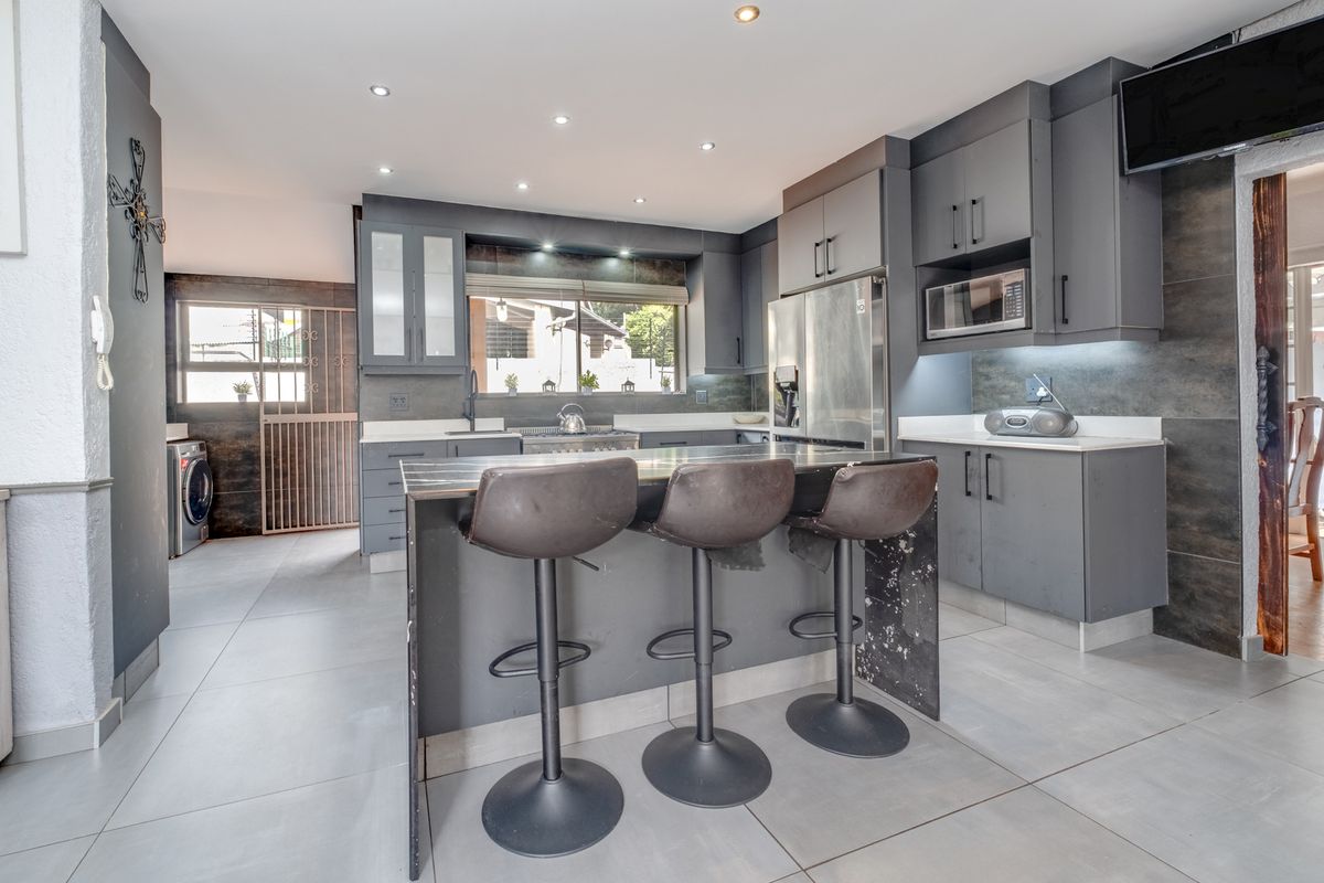 Modern kitchen featuring dark grey cabinetry, stone countertops, a central island with breakfast bar seating, and integrated appliances with recessed lighting.