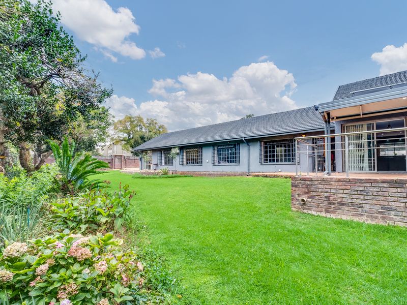Rear view of the house featuring a well-maintained lawn, landscaped garden, and a brick patio with stainless steel railings.
