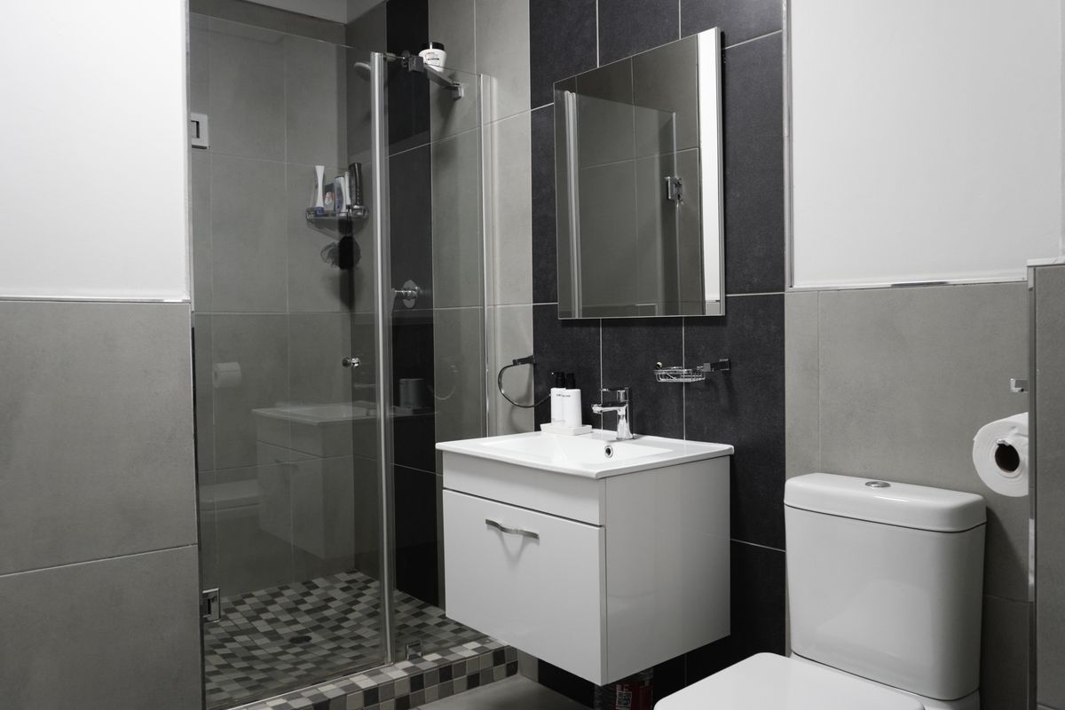 Modern bathroom featuring a glass-enclosed shower, wall-mounted vanity with basin, and contemporary tiled finishes.