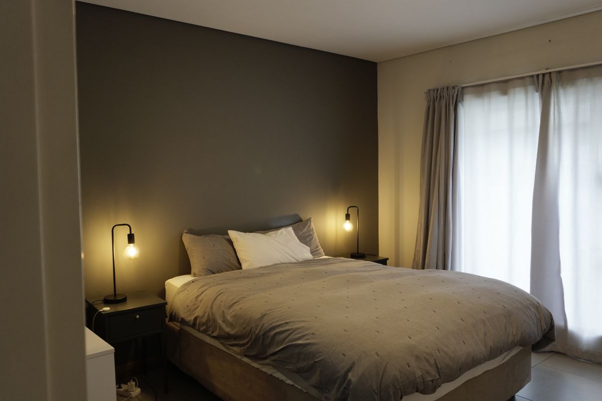 A well-lit bedroom featuring a neutral color palette, a feature wall, and direct access to an outdoor area through a sliding glass door.