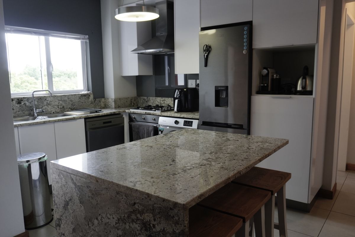 Modern kitchen featuring granite countertops, a central island, built-in oven, gas hob, and sleek white cabinetry with integrated appliances.