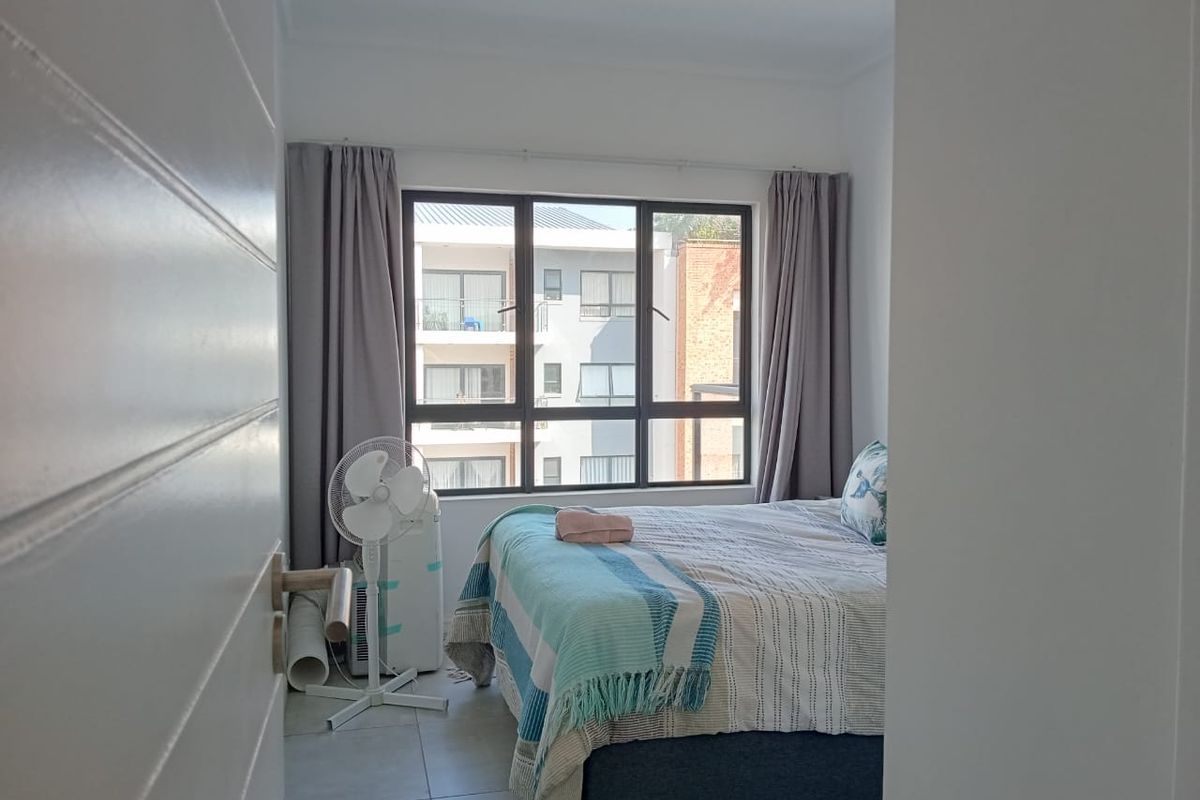 A bedroom featuring tiled flooring and large windows that provide natural light and a view of the surrounding apartment complex.