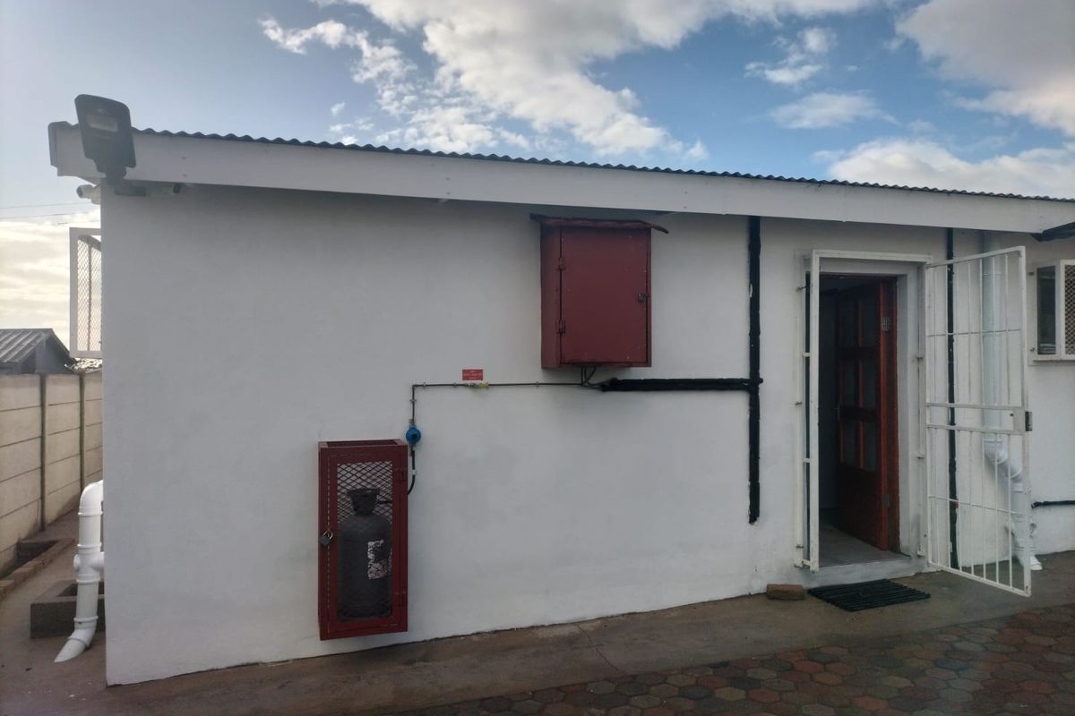Exterior view of the property showing a utility area with a gas cylinder cage, electrical box, and security gate access.