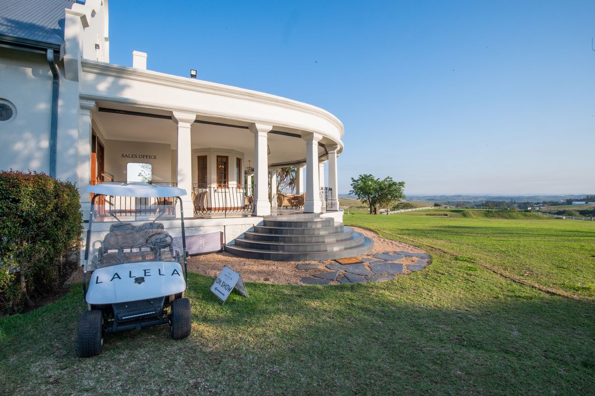 A well-maintained covered patio with stone steps and columns, overlooking a spacious green lawn and expansive landscape views.
