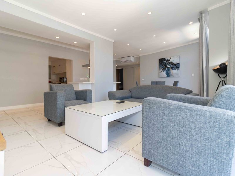 Spacious open-plan living area featuring modern porcelain floor tiles, recessed downlighting, and a wall-mounted air conditioning unit.