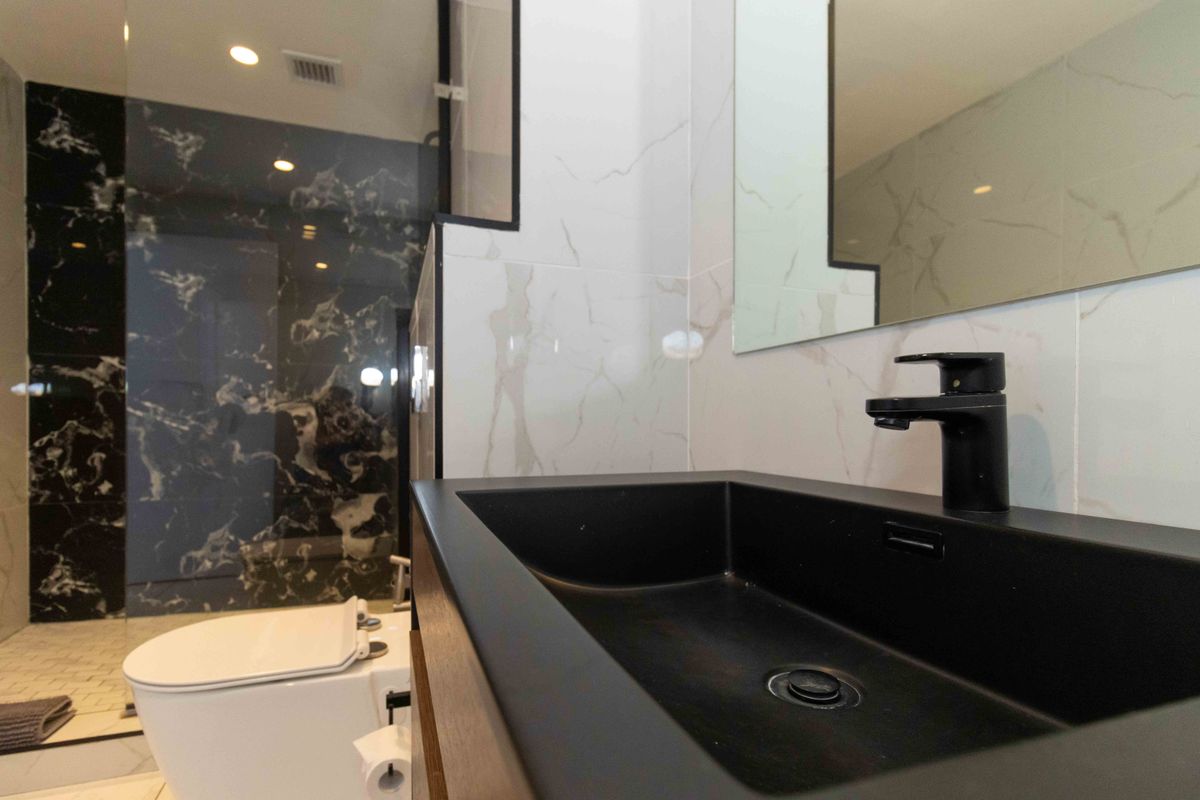 Modern bathroom featuring a sleek black matte basin, wall-mounted toilet, glass shower enclosure, and elegant marble-effect wall tiling.
