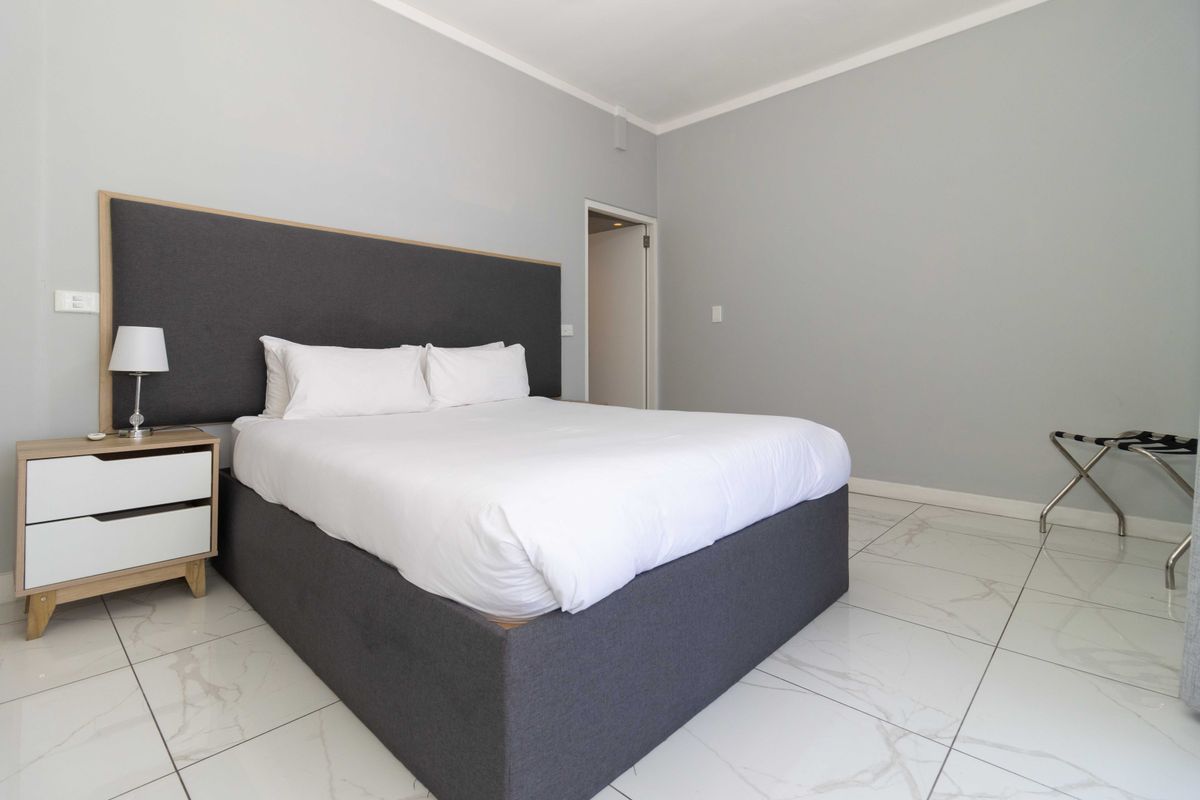 A clean and modern bedroom featuring large-format marble-look floor tiles, neutral grey walls, and a built-in headboard design.
