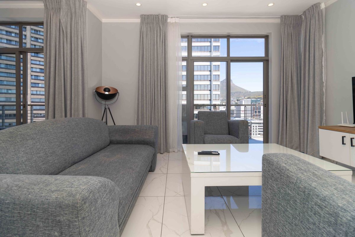 Modern living room featuring large windows, tiled flooring, and recessed downlights, offering bright natural light and access to a balcony with city views.