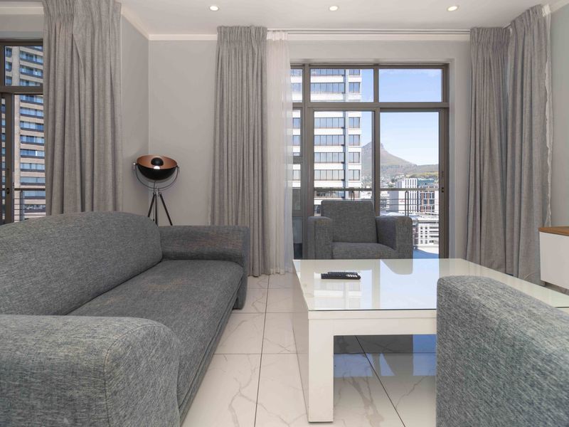 Modern living room featuring large windows, tiled flooring, and recessed downlights, offering bright natural light and access to a balcony with city views.