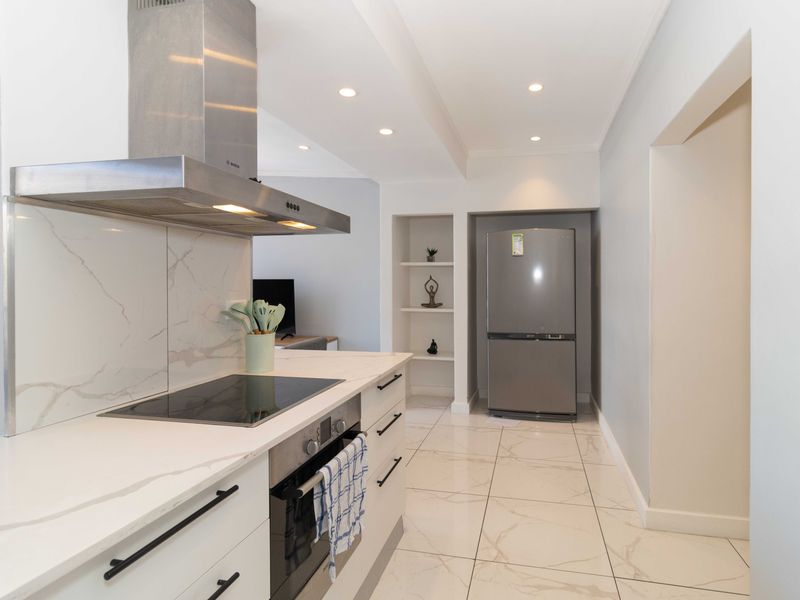 Modern kitchen featuring marble-look quartz countertops, integrated stainless steel appliances, sleek cabinetry, and polished tiled flooring with recessed lighting.