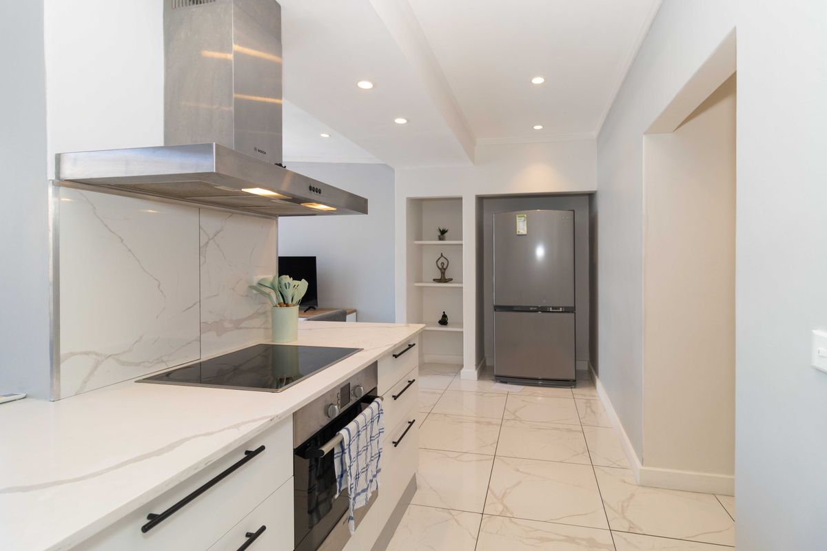 Modern kitchen featuring marble-look quartz countertops, integrated stainless steel appliances, sleek cabinetry, and polished tiled flooring with recessed lighting.