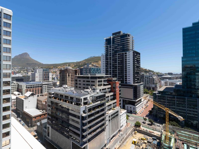 An elevated urban cityscape view showcasing surrounding high-rise buildings and distant mountain scenery.