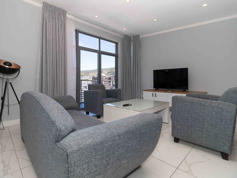A well-maintained living room featuring modern tiled flooring, recessed downlights, and a large sliding glass door providing natural light and access to the balcony.