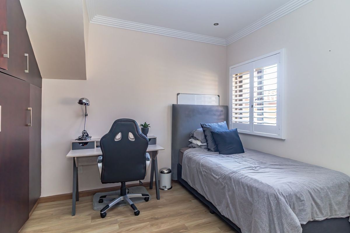 A well-maintained bedroom featuring built-in dark wood cabinetry, light wood-look flooring, and white plantation shutters on the window.