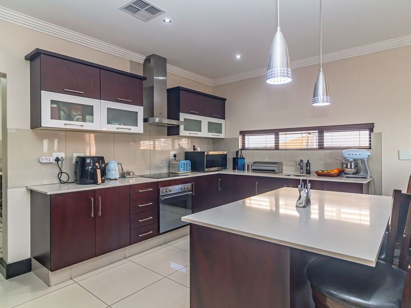 Modern kitchen featuring dark wood cabinetry, stone countertops, a central island, stainless steel appliances, and tiled flooring, with an adjacent scullery area.