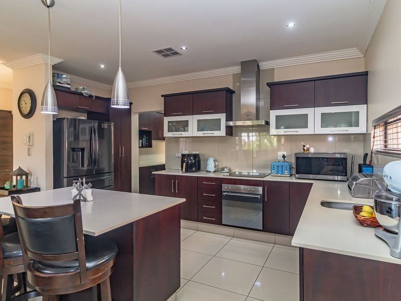 Modern kitchen featuring dark wood cabinetry, stone countertops, stainless steel appliances, a central island with breakfast bar seating, and recessed ceiling lighting.