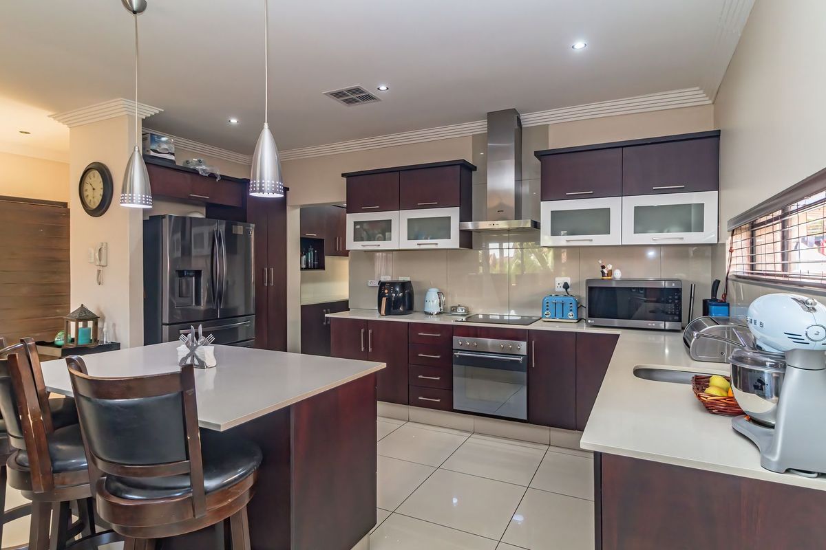 Modern kitchen featuring dark wood cabinetry, stone countertops, stainless steel appliances, a central island with breakfast bar seating, and recessed ceiling lighting.