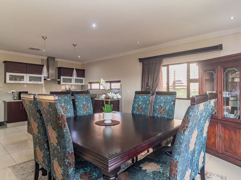 Open-plan dining area featuring tiled flooring and recessed lighting, seamlessly connected to a modern kitchen with dark cabinetry and stainless steel extractor fan.