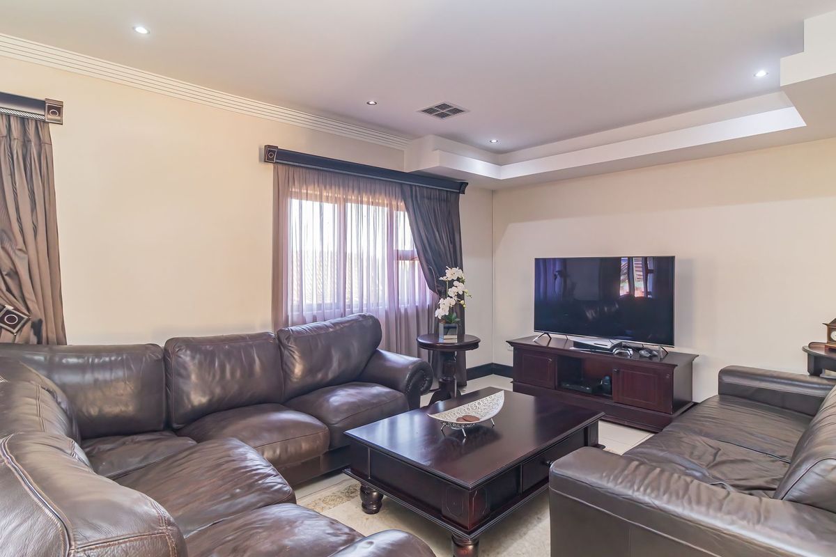 A comfortable living room featuring recessed ceiling lighting, a tray ceiling design, and large windows with fitted curtain tracks.