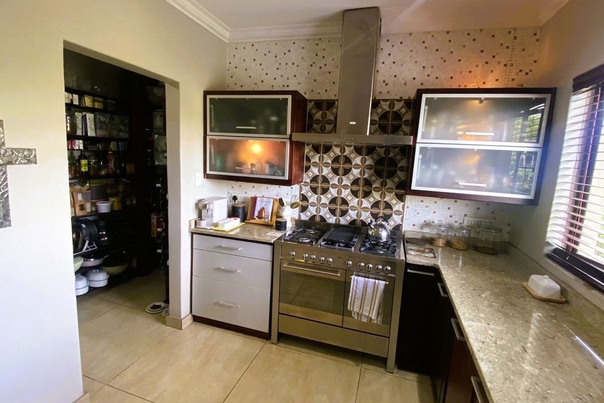 A well-appointed kitchen featuring granite countertops, a stainless steel gas range with extractor hood, decorative mosaic backsplash, and an adjacent walk-in pantry.