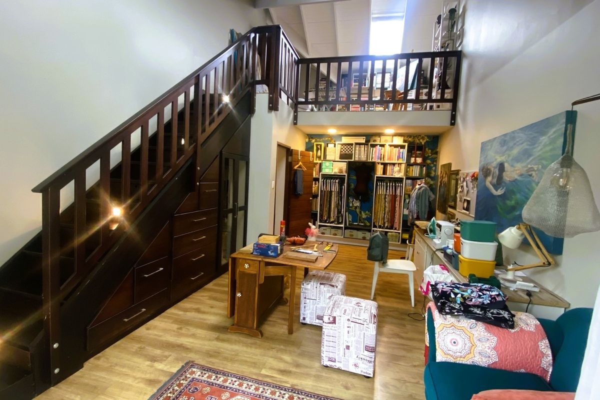 A versatile living space featuring a dark wood staircase with integrated under-stair storage and a mezzanine loft level with a wooden balustrade.