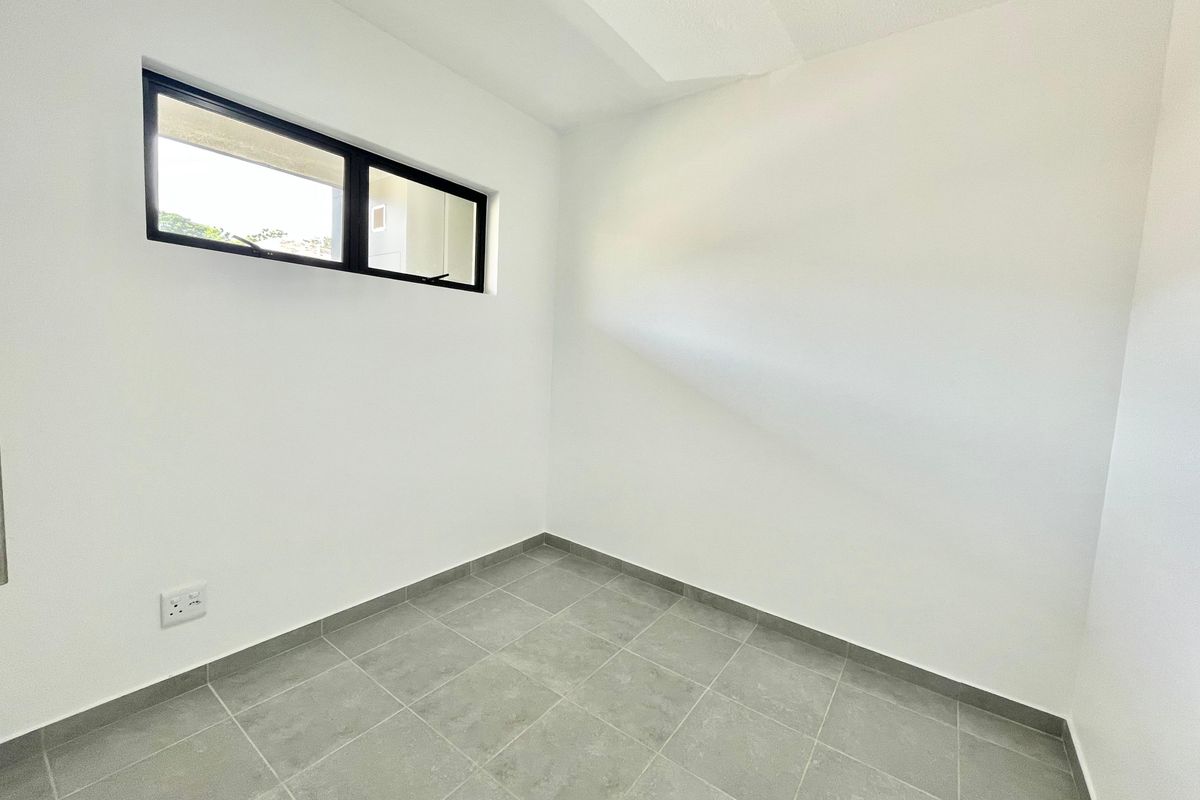 A clean, empty room featuring neutral grey floor tiles, white walls, and a modern black-framed window, suitable for a bedroom or home office.