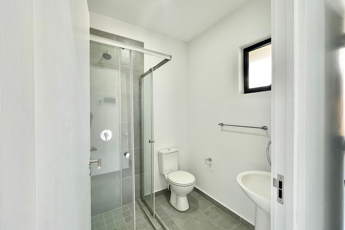 A modern, clean bathroom featuring a glass-enclosed shower, pedestal basin, and toilet with neutral grey floor tiling.