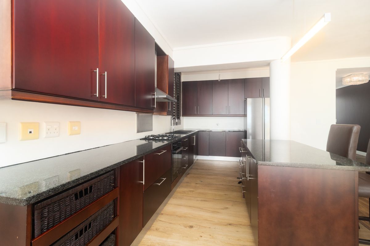 Modern kitchen featuring dark wood cabinetry, granite countertops, a built-in gas hob, and an integrated island breakfast bar.