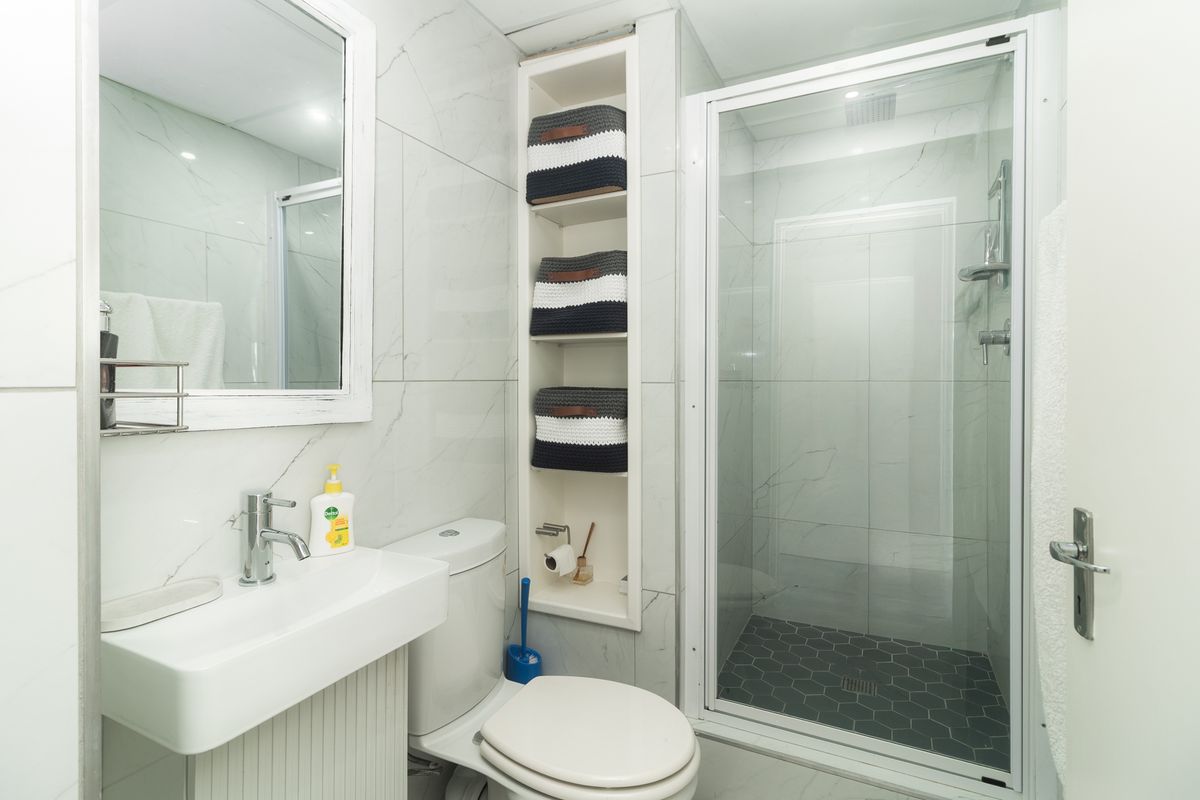 Modern bathroom featuring marble-look wall tiles, a glass-enclosed shower with dark hexagonal floor tiles, a wall-mounted vanity, and built-in shelving.